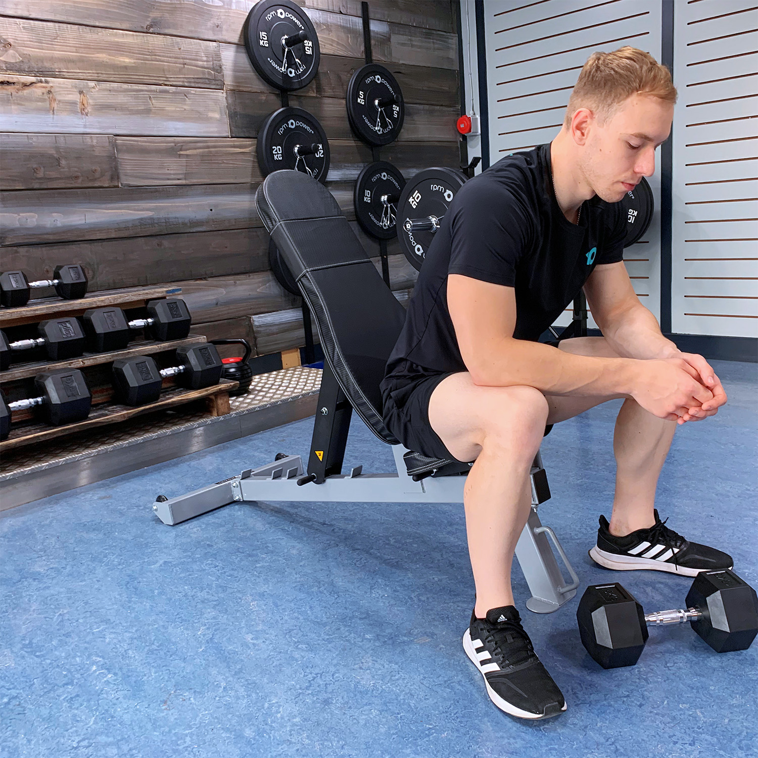 Man sitting on weight bench with dumbbell at his feet and behind him