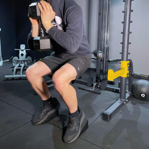 man holding hexagonal dumbbell squatting on wedge platform