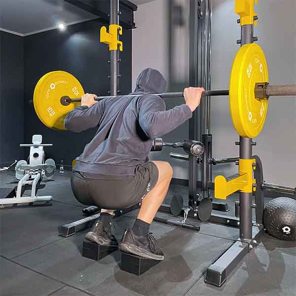 man holding barbell and bumper plates squatting on squat wedges