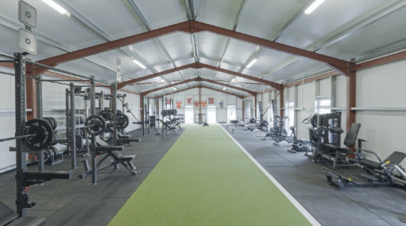 A wide shot of a large gym with green turn flooring and equipment